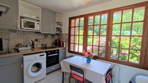 A compact kitchen with a washing machine, a microwave, and a dining area with a table and chairs. - Holiday Home 'Gite Les Rosiers' with Private Garden (Eu)