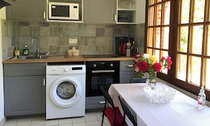 A compact kitchen with a washing machine, oven, microwave, and a dining area with a table and chairs. - Holiday Home 'Gite Les Rosiers' with Private Garden (Eu)