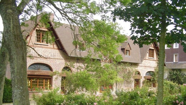 A traditional brick house with a sloped roof, arched windows, and a well-maintained garden with flowering plants. - Holiday Home 'Gite Les Rosiers' with Private Garden (Eu)