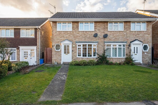 A two-story brick house with a front garden, a pathway leading to the entrance, and a satellite dish on the roof. - Charming 3 Bed Hse Family and Long Stay (Maidenhead)