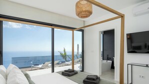 Ein modernes Schlafzimmer mit einem großen Bett, einem Fernseher und einem Balkon mit Meerblick.