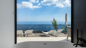 Ein Balkon mit Meerblick, einer weißen Badewanne und zwei Liegestühlen.