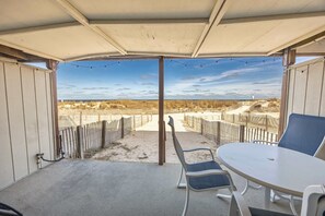 Eine Terrasse im Freien mit Tisch und Stühlen, einem überdachten Bereich und Blick auf den Strand.
