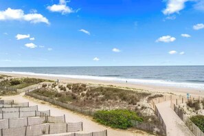 Blick auf einen Strand mit Holzzaun, Sandweg und dem Meer.