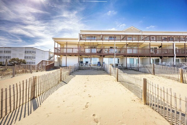 Ein Hotel direkt am Strand mit einer zweistöckigen Struktur, einem Sandstrand davor und einem Holzzaun.