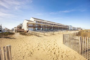Een strandhotel met meerdere balkons, een zandstrand ervoor en een houten omheining.