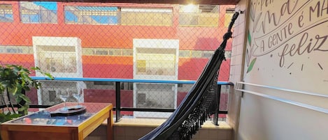 A balcony with a hammock, a table with glasses, and a wall with a message.
