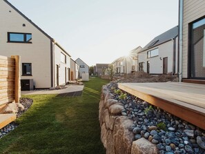 A modern residential area with white buildings, a grassy pathway, and a wooden deck. - 4 Star Holiday Home in Sagad (Sagard)
