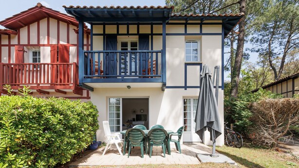 Una casa de dos pisos con un balcón, un patio con sillas y una mesa, y una bicicleta estacionada afuera.
