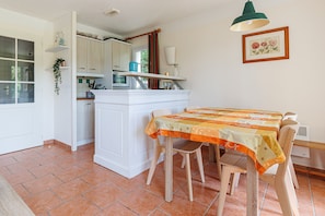 Una cocina con armarios blancos, una mesa de comedor con sillas y una lámpara colgante verde.