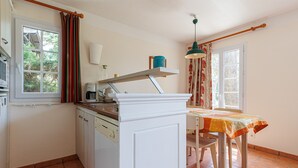 Una cocina con mostrador blanco, cafetera, estante y mesa de comedor con mantel.