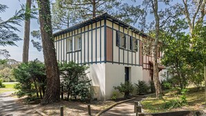 Un edificio tradicional con fachada blanca y detalles oscuros, rodeado de árboles y un camino de grava.