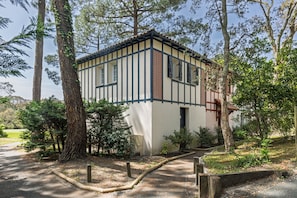 Un edificio tradicional con fachada blanca y detalles oscuros, rodeado de árboles y un camino de grava.