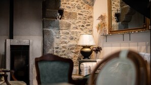 A stone wall, a fireplace, a lamp, and a mirror in a room. - LE COTTAGE - Charming gîte at the foot of the Château (Combourg)