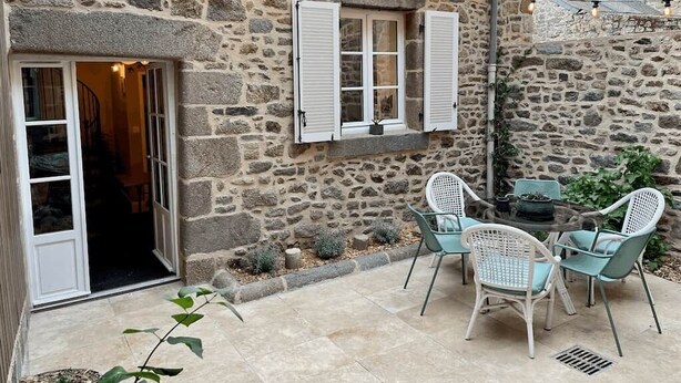 A stone building with a patio area, outdoor seating, and string lights. - LE COTTAGE - Charming gîte at the foot of the Château (Combourg)