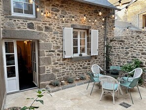 A stone building with a patio area, outdoor seating, and string lights. - LE COTTAGE - Charming gîte at the foot of the Château (Combourg)