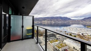 A balcony with a view of a lake and mountains. - Modern 1-bedroom condo, Lakeview, sleeps 4,  pool, gym, amazing amenities. (Kelowna)