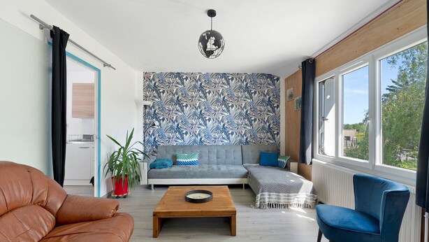 Ein Wohnzimmer mit einer Couch, einem blauen Sessel, einem Couchtisch und einer Wand mit Muster.