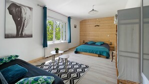 Ein Schlafzimmer mit Bett, Schreibtisch, Stuhl, einem Fenster mit Vorhängen, einem Heizkörper und einem Wandbild.