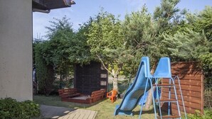 Un jardin avec une terrasse en bois, un toboggan et une échelle.