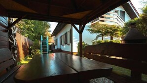Un espace extérieur aménagé en terrasse, avec une table et des bancs en bois, entouré d’une clôture en bois et avec un bâtiment visible au fond.
