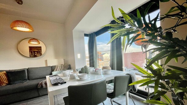 Ein modernes Wohnzimmer mit Essbereich, einer Couch, einem Tisch mit Stühlen und einem großen Fenster mit Aussicht.