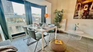 Ein modernes Wohnzimmer mit Essbereich, großen Fenstern, einem Topf mit Pflanze und einem Tiger-Kunstwerk an der Wand.