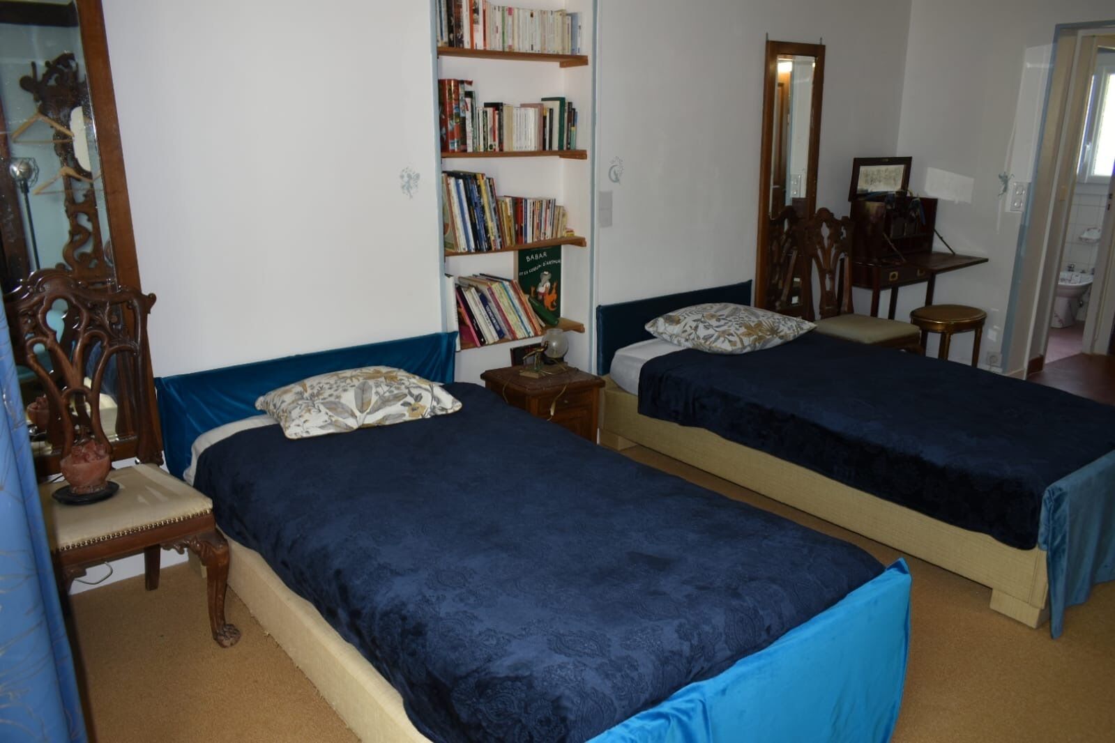 Una habitación con dos camas, una estantería, un espejo y un escritorio.