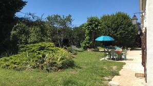 A garden with a dining area, a blue umbrella, and a pathway leading to a building.