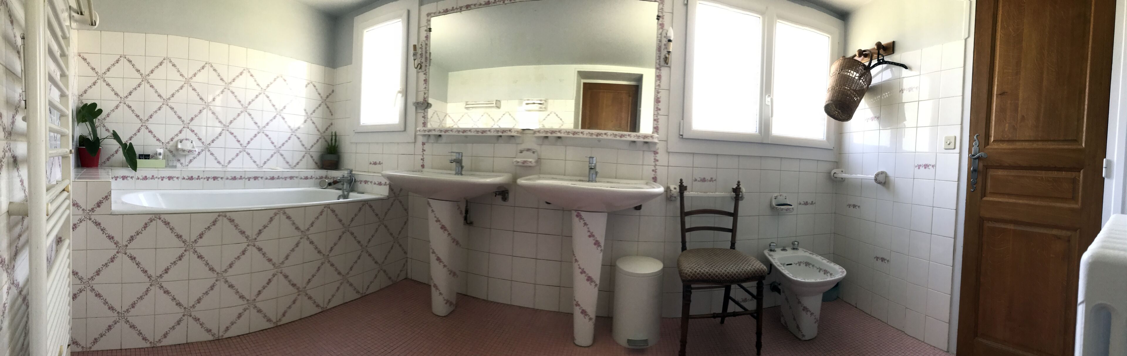Un baño con una bañera grande, dos lavamanos, un espejo, una silla y un inodoro.