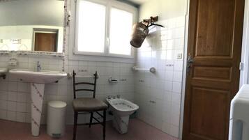 Un baño con una bañera grande, dos lavamanos, un espejo, una silla y un inodoro.