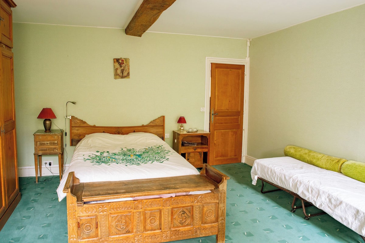 A bedroom with a wooden bed, a bedside table, a nightstand, a green carpet, and a door.