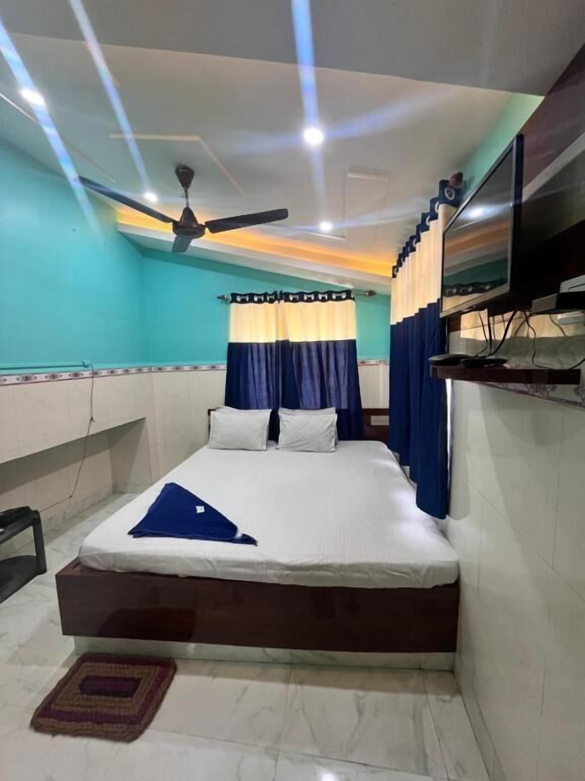 Un dormitorio con una cama, un ventilador de techo, un televisor montado en la pared y una ventana con cortinas.