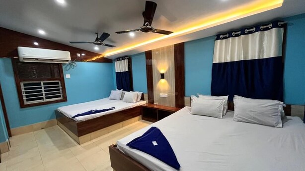 Een hotelkamer met twee bedden, plafondventilatoren, een airconditioning en een raam met jaloezieën.
