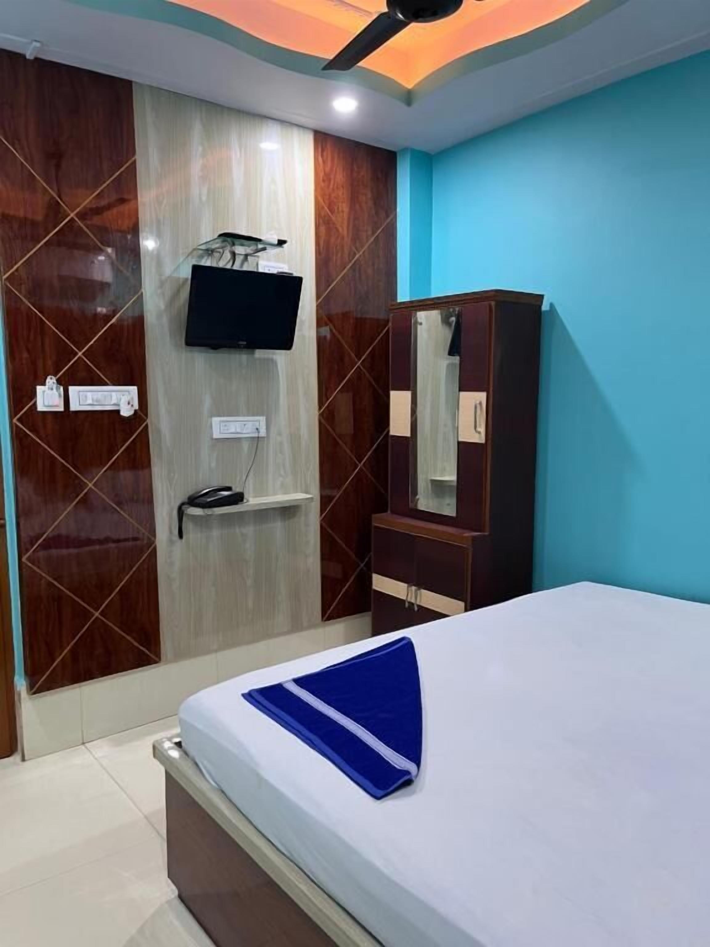 A bedroom with a bed, a TV mounted on a wall, a wardrobe, and a ceiling fan.