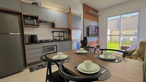 A modern kitchen with built-in appliances, a dining area with a table set for four, and a large sliding glass door to a balcony. - Jardim dos Corais - Miramar (João Pessoa)
