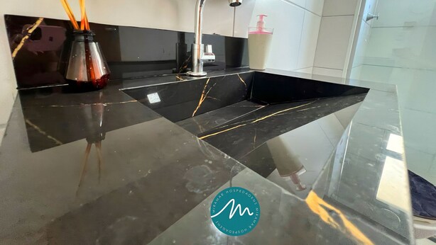 A modern kitchen with a black marble countertop, a stainless steel sink, and a faucet. There are wooden sticks in a glass container on the left. - Jardim dos Corais - Miramar (João Pessoa)