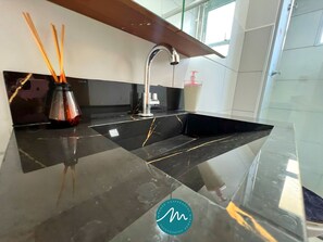 A modern kitchen with a black marble countertop, a stainless steel sink, and a faucet. There are wooden sticks in a glass container on the left. - Jardim dos Corais - Miramar (João Pessoa)