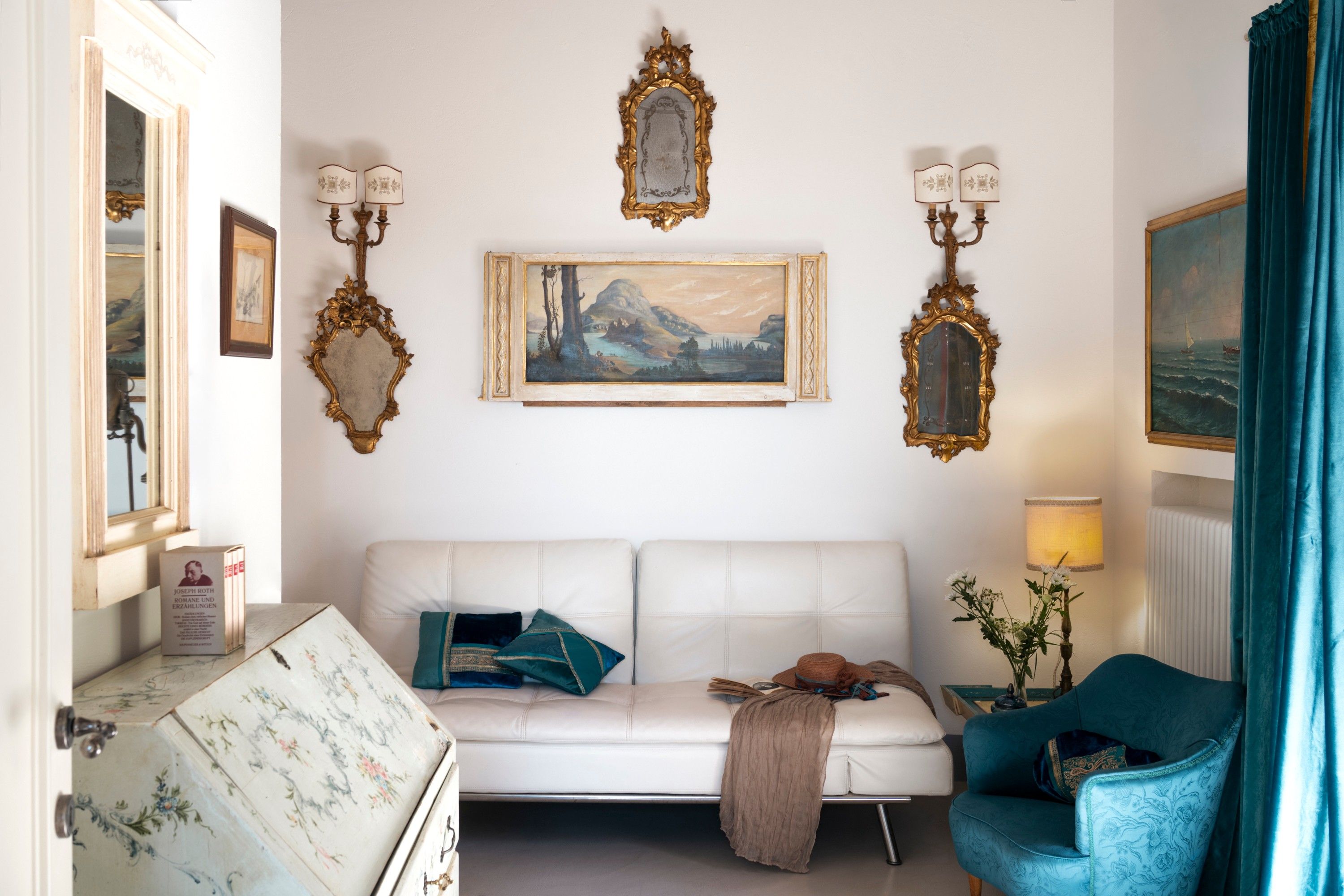 Une pièce avec un canapé blanc, un fauteuil bleu et un tableau accroché au mur.