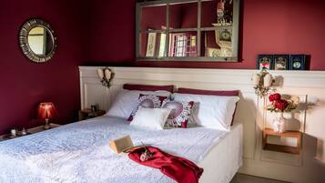 A neatly made bed with a white bedspread and red throw, a bedside table with a lamp, and a wall-mounted mirror.