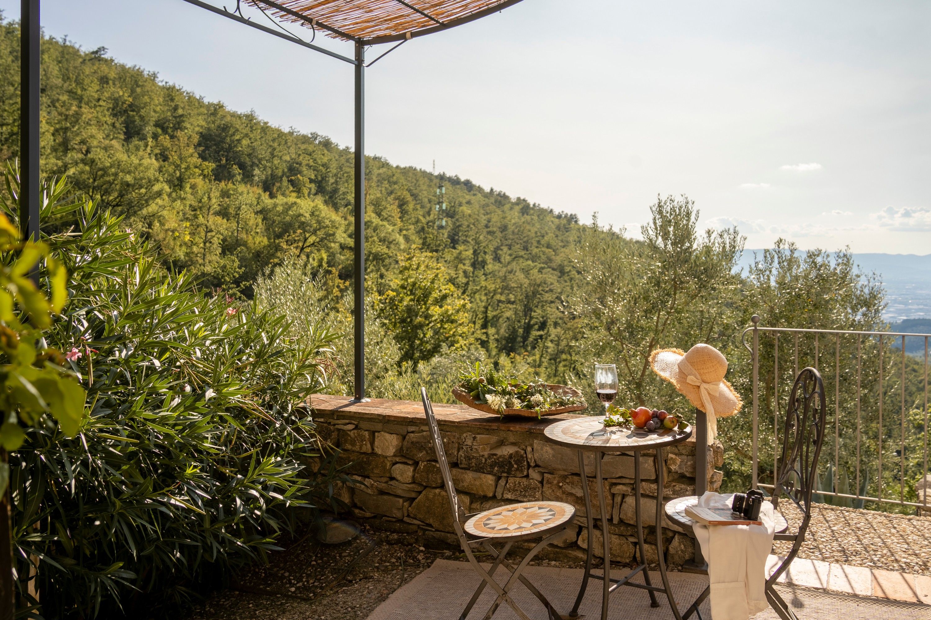 Un patio exterior con una mesa de piedra, dos sillas, una copa de vino y una cesta de fruta.