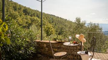 Un patio exterior con una mesa de piedra, dos sillas, una copa de vino y una cesta de fruta.