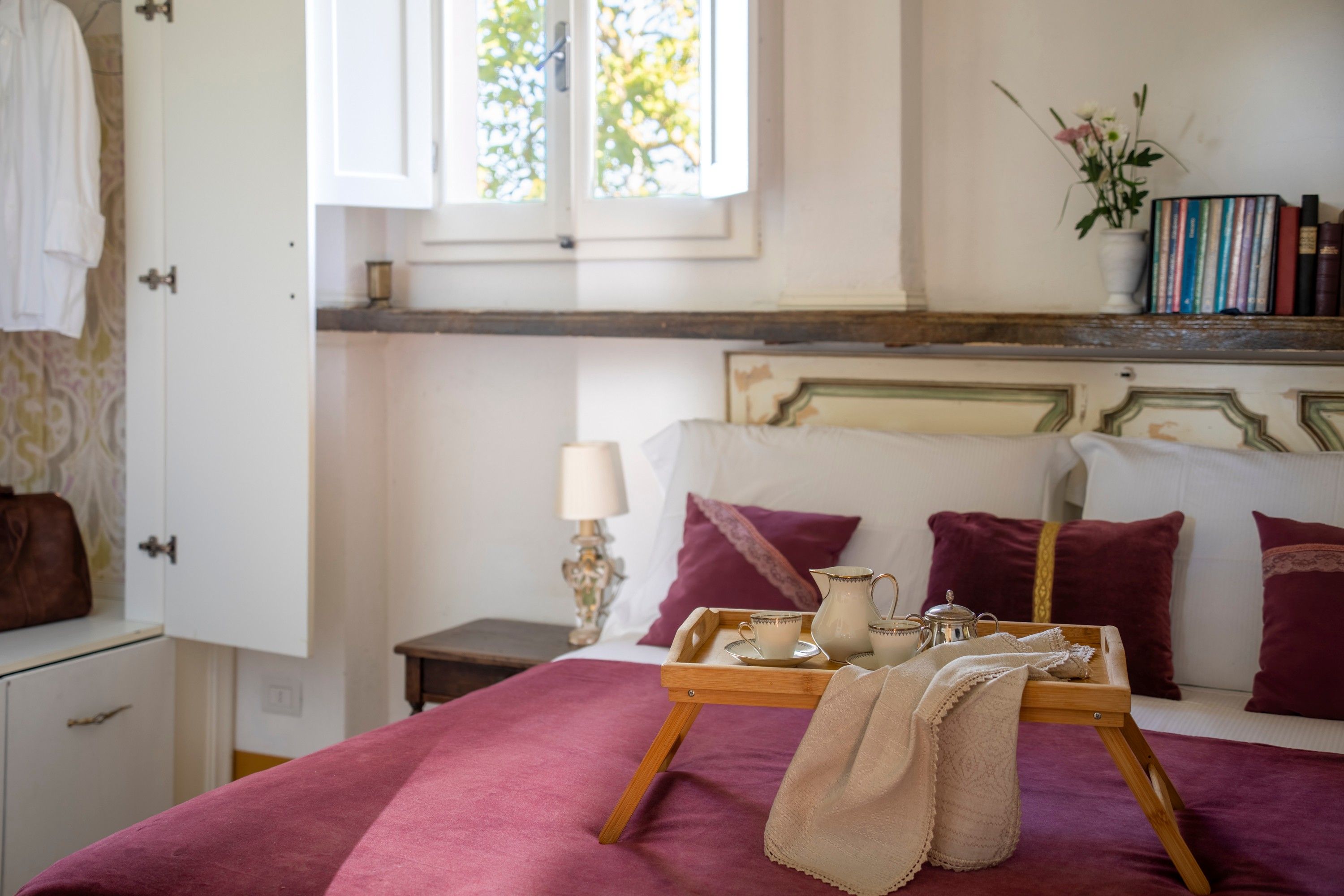 A bedroom with a bed, a bedside table, a window, and a shelf with books.