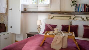 A bedroom with a bed, a bedside table, a window, and a shelf with books.