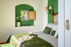 Ein Schlafzimmer mit grüner Wand, einem Fenster mit einem Bild, einem Nachttisch mit Lampe und einem Bett mit grüner Bettwäsche.