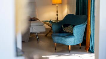 A room with a blue armchair, a white sofa, a lamp, and a window with curtains.