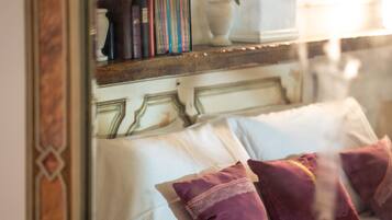Una cama con almohadas, un cabecero y un estante con libros y una planta.
