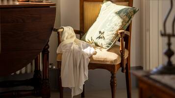 Una silla de madera con un cojín y un paño blanco cubriéndola, ubicada cerca de una ventana con marco rojo.