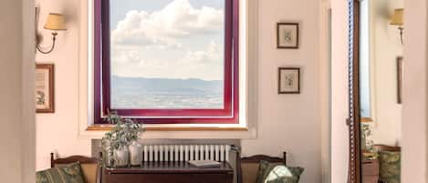 Ein Zimmer mit einem großen Fenster, einem Holztisch, zwei Stühlen, einem Heizkörper und gerahmten Bildern an der Wand.