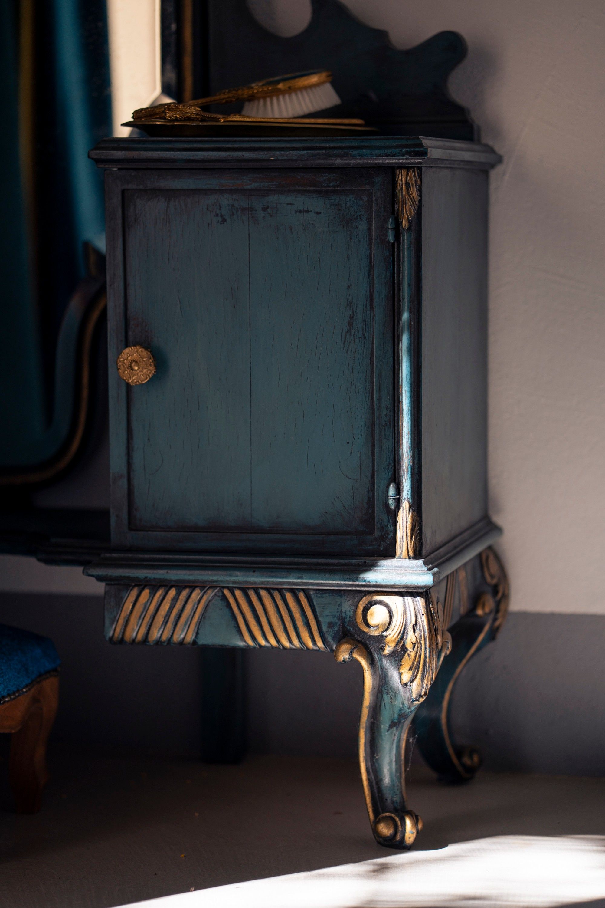 A dark blue cabinet with ornate gold detailing and a brass knob.